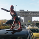 Tom Holland's Peter Parker crouches atop a car in traffic in his Iron Spider armor, ready for battle in Spider-Man: No Way Home.